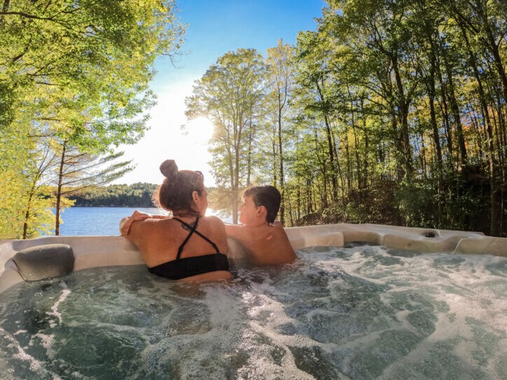 Mutter und Sohn entspannen im Outdoor-Whirlpool und blicken dabei auf einen See