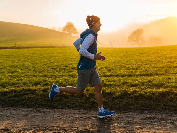 Ein junger Mann joggt im Morgengrauen an einer Wiese entlang