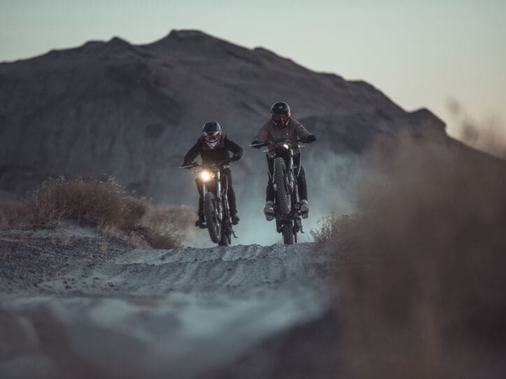 Zwei Motorradfahrer fahren in der Dämmerung durch eine Wüstenlandschaft