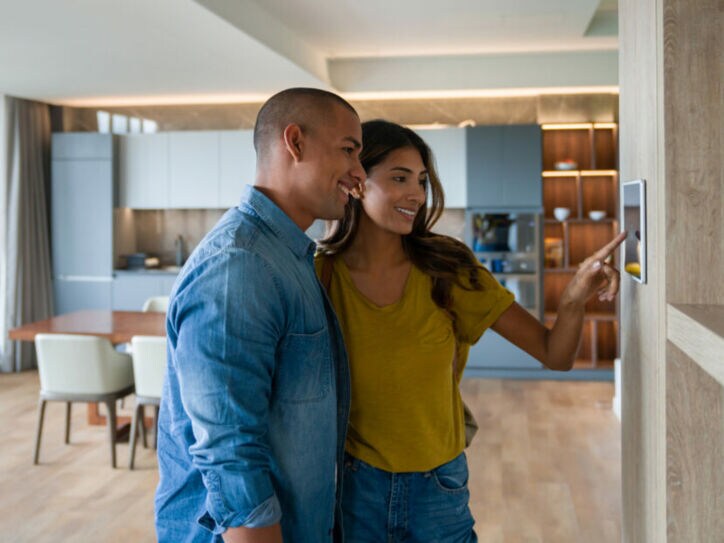 Zwei Personen stehen in einer modern eigenrichteten Wohnung und bedienen einen Touchscreen an der Wand