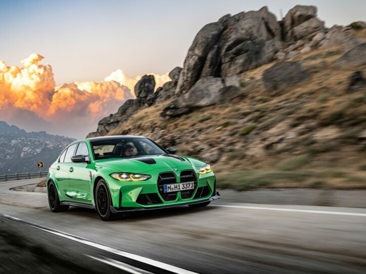 Ein grüner BMW auf einer Landstraße, im Hintergrund große Wolken und Berge