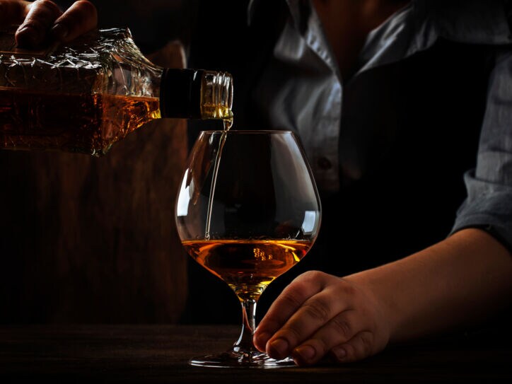 Ein Barkeeper hinter einer dunklen Holztheke gießt Cognac in ein bauchiges Glas