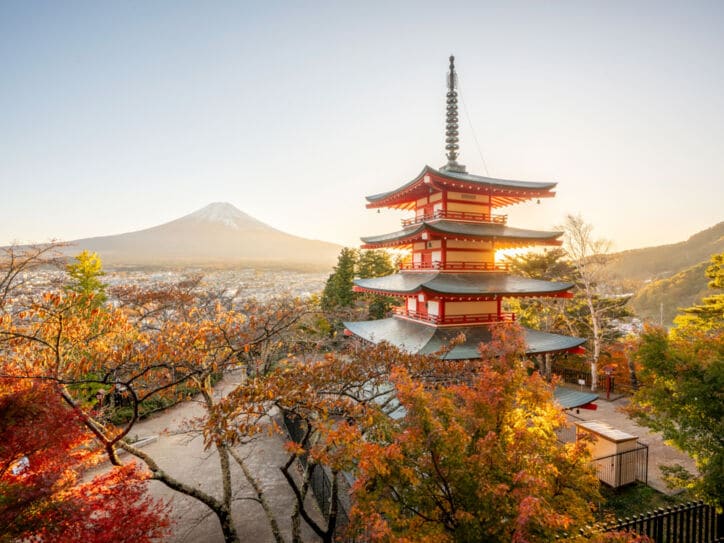 Ein mehrstöckiger, japanischer Tempel mit roten Ornamenten, im Hintergrund eine Stadt am Fuße des Mount Fuji