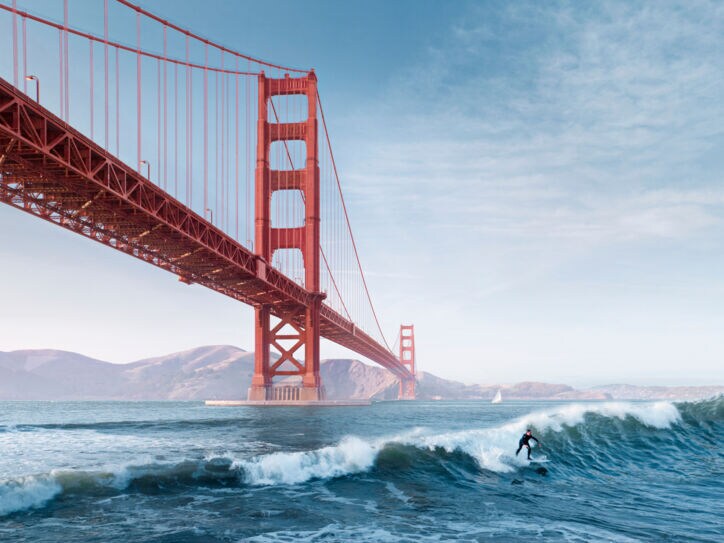 Ein Surfer auf einer Welle unter der roten Golden Gate Bridge