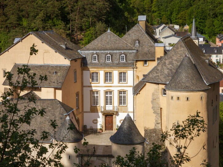 Kleine Burg aus beigem Sandstein mit Rundtürmen und Innenhof in einem bewaldeten Gebiet