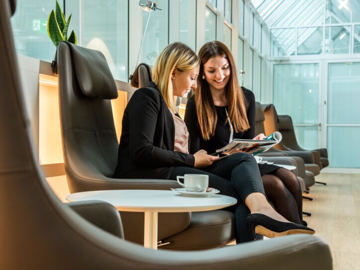 Zwei Frauen auf Ledersesseln schauen gemeinsam auf ein Magazin in einer Lounge.