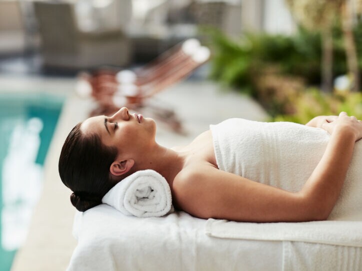 Eine Frau entspannt in einem weißen Handtuch auf einer Massageliege an einem Hotelpool.