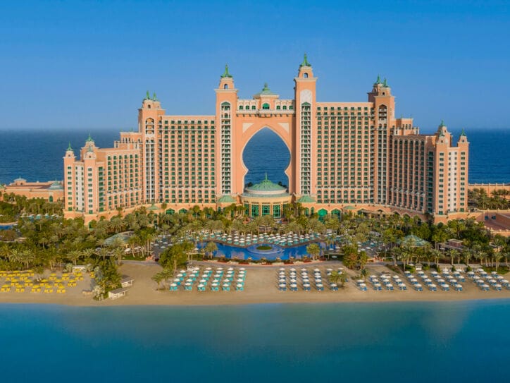 Großer Hotelkomplex im arabischen Stil auf einer Landzunge mit Sandstrand, umgeben von blauem Wasser.