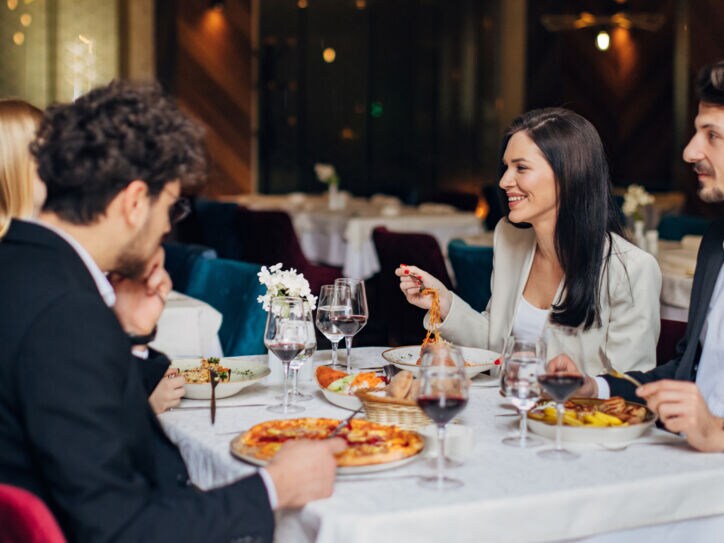 Vier elegant gekleidete Personen sitzen beim Essen an einem Tisch in einem Restaurant.