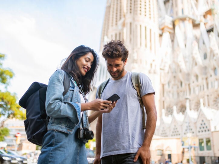 Zwei Personen stehen in Barcelona vor der Sagrada Família und blicken zusammen auf ein Smartphone.