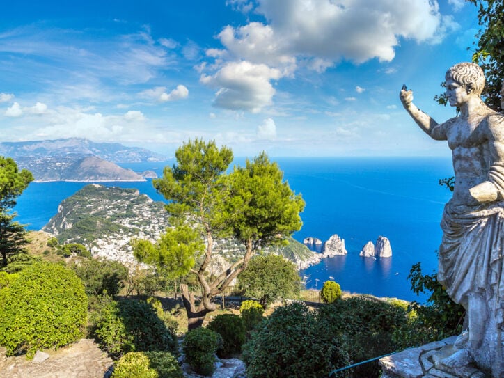 Landschaftspanorama der Insel Capri im blauen Meer, im Vordergrund eine Steinstatue in einem Park.