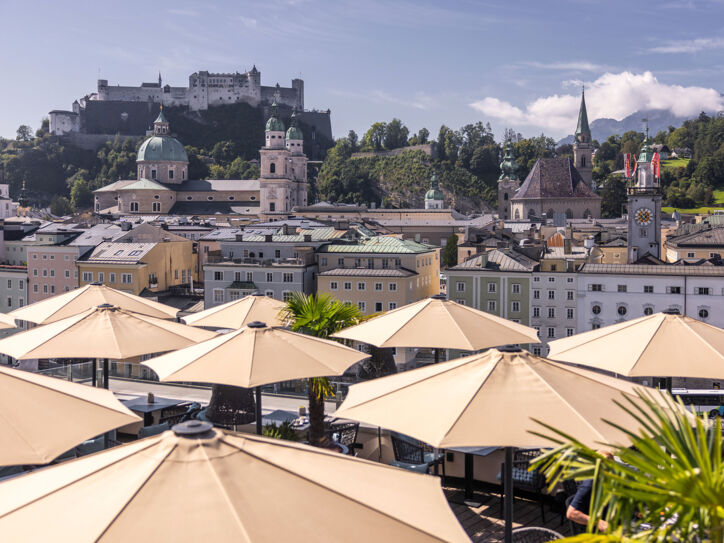 Panorama der Salzburger Altstadt mit Burg auf einem Berg am Fluss, im Hotelterrasse mit Sonnenschirmen.