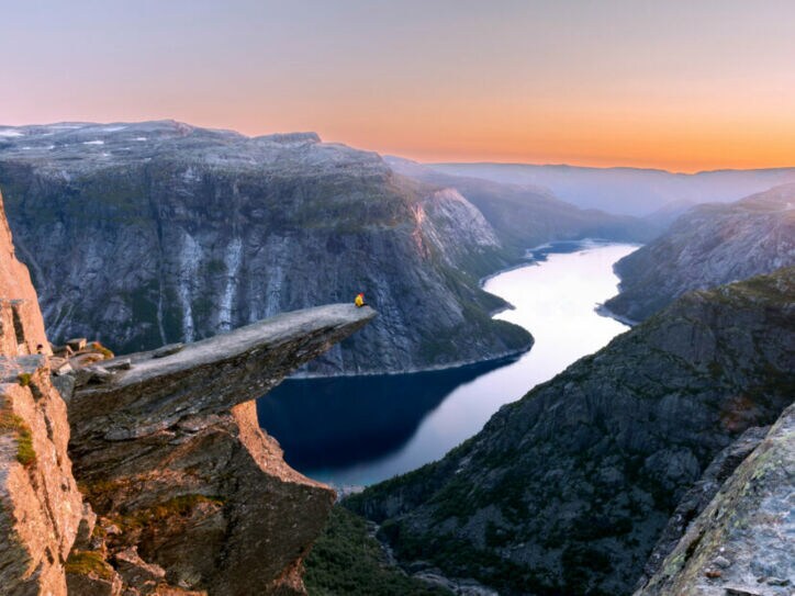 Fjordlandschaft mit Person auf einer Felsklippe bei Sonnenuntergang.