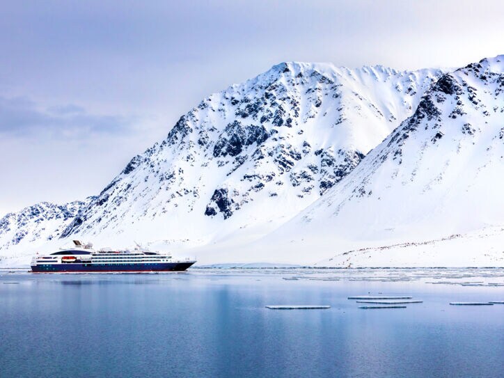 Ein Expeditionsschiff im arktischen Gewässer vor schneebedeckten Bergen.