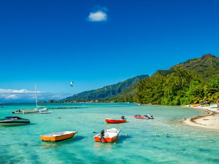 Kleine Boote im türkisblauen Wasser an einem Sandstrand mit tropischer Vegetation.