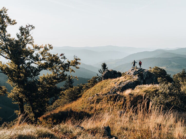 Zwei Personen stehen auf einem Felsen und blicken in die Ferne, im Hintergrund Gipfel im Schwarzwald.