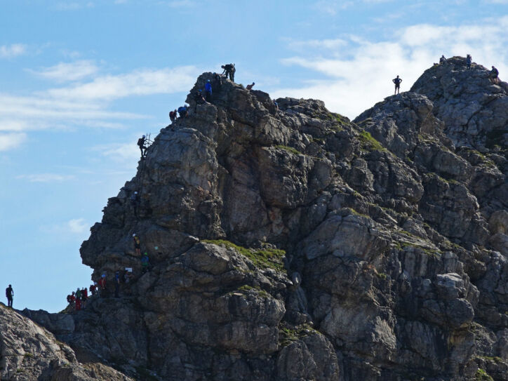 Mehrere Personen, die einen Felsen am Hindelanger Klettersteig erklimmen.