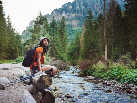 Eine Frau sitzt mit Wanderausrüstung an einem Bach im Wald