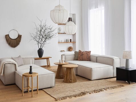 Ein lichtdurchflutetes, modernes Wohnzimmer im skandinavischen Design mit einer kubischen Sitzgruppe aus grauem Stoff und dekorativen Wohnaccessoires