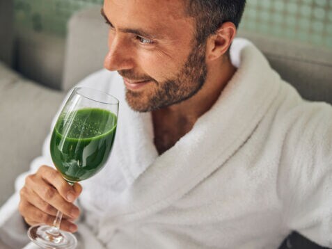 Mann in Bademantel, der ein Glas mit grünem Inhalt in der Hand hält