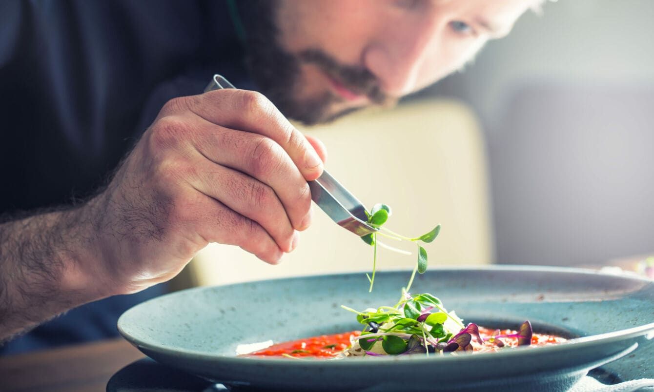 Ein Küchenchef richtet mit der Hand die Tomatensuppe an