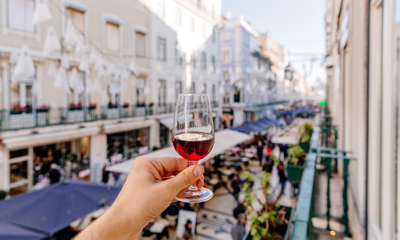 Eine Hand hält ein Glas Portwein oberhalb einer belebten Gasse in die Luft