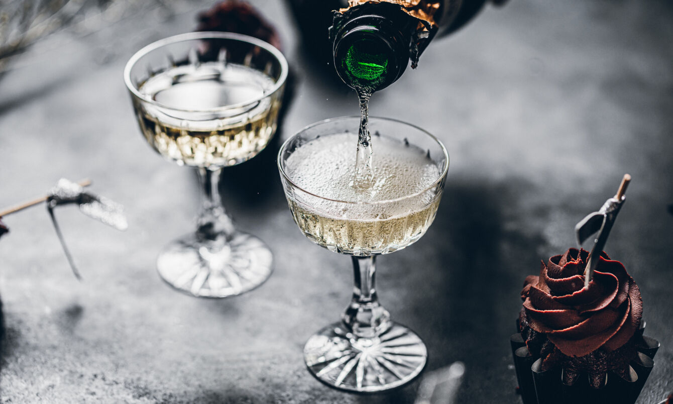 Zwei Gläser auf einem grauen Tisch werden mit Champagner gefüllt, daneben ist ein Cupcake mit Schokohaube zu sehen