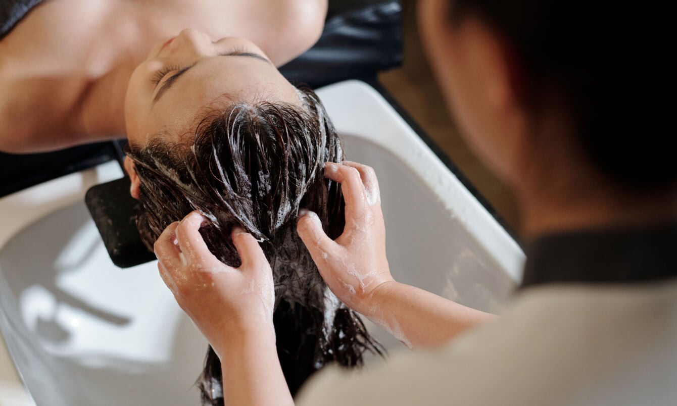 Die Haare einer liegenden Frau werden an einem Waschbecken von einer anderen Person gewaschen.