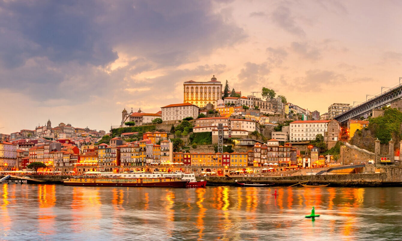 Panoramaaufnahme der Stadt Porto bei Sonnenuntergang mit dem Fluss Duoro im Vordergrund.