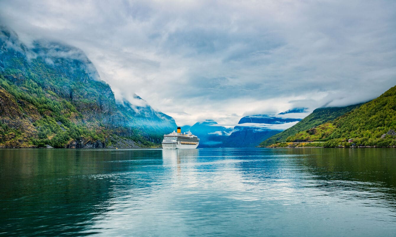 Kreuzfahrtschiff in wolkenverhangener Fjordlandschaft.