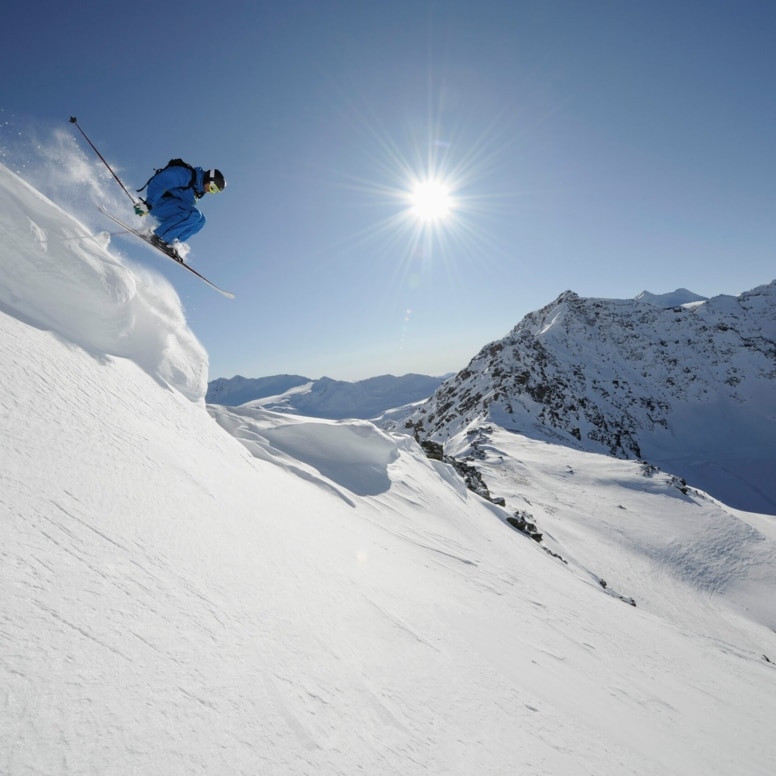 Skifahrer:in springt von einer Klippe, Sonne und Schnee