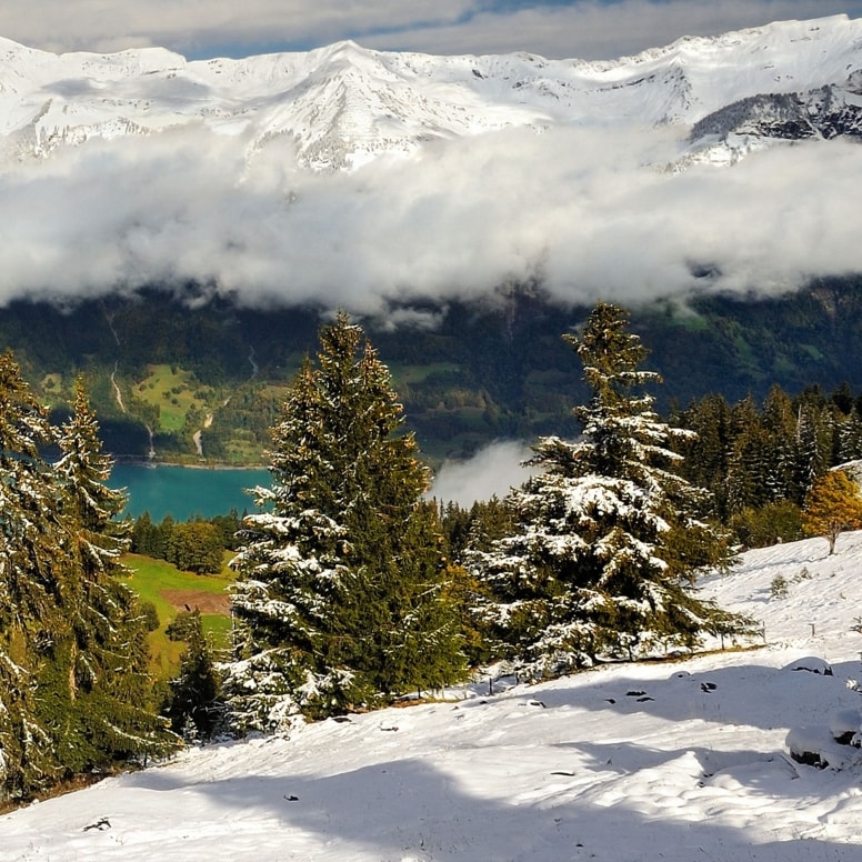 Schneebedeckte Berge, ein Bergsee und tiefhängende Wolken