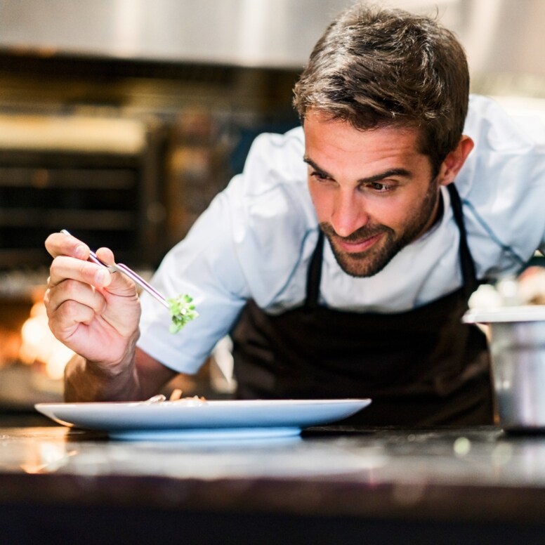 Ein Mann garniert ein Gericht auf einem weißen Teller in einer Restaurantküche.