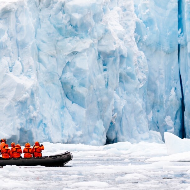 Ein Schlauchboot mit mehreren Personen vor einer gigantischen Eiswand