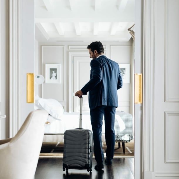 Ein junger Geschäftsmann mit Rollkoffer in einer hellen, luxuriösen Hotelsuite