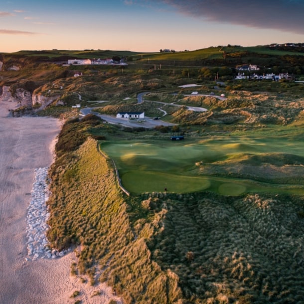 Blick auf einen Golfplatz und einen Küstenstreifen mit Sandstrand aus der Luft