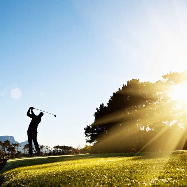 Die Silhouette eines ausholenden Golfspielers im Gegenlicht auf einem Golfplatz
