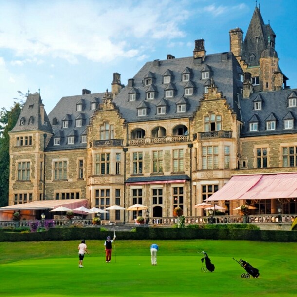 Außenaufnahme von Schlosshotel mit Terrasse, davor Rasen mit Golfenden