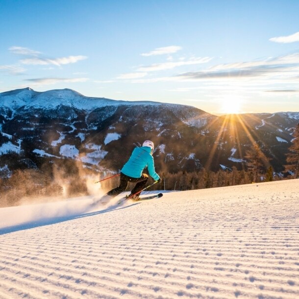 Eine Person auf Ski fährt bei Sonnenschein eine Piste hinab.
