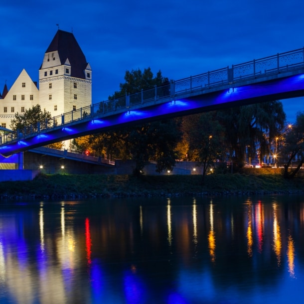 Das beleuchtete Neue Schloss in Ingolstadt bei Nacht, im Vordergrund führt eine Brücke über die Donau