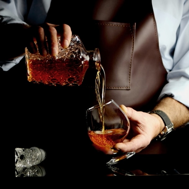 Ein Mann gießt Cognac aus einer Flasche ins Glas.