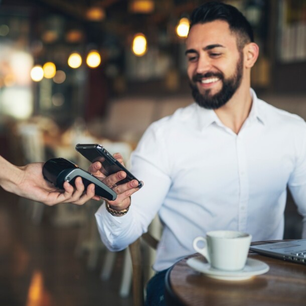 Ein junger Mann bezahlt kontaktlos mit seinem Smartphone in einem Café