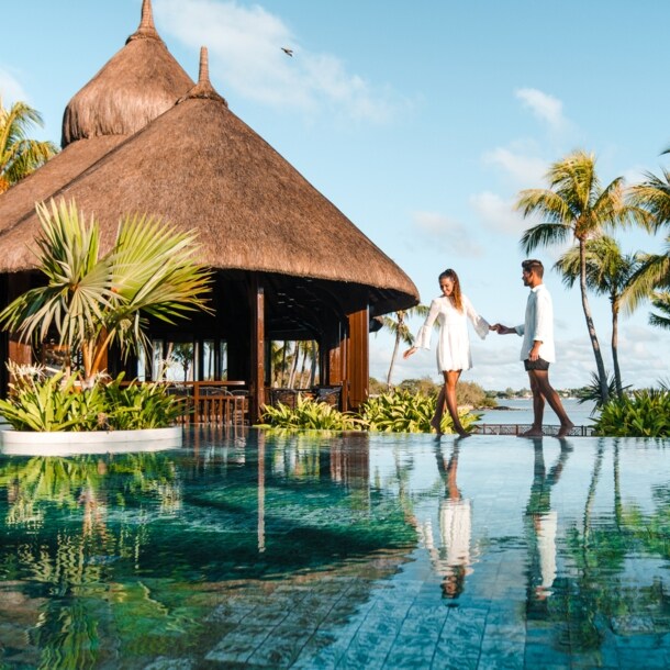 Ein Paar steht an einem luxuriösen Hotelpool am Meer in tropischer Umgebung.