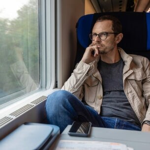 Mann sitzt in fahrendem Zug und schaut aus dem Fenster.