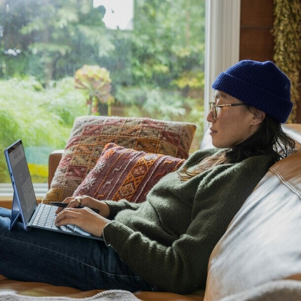 junge Frau sitzt gemütlich mit Laptop auf dem Sofa