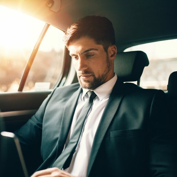 Geschäftsmann sitzt mit Laptop auf dem Rücksitz eines Autos