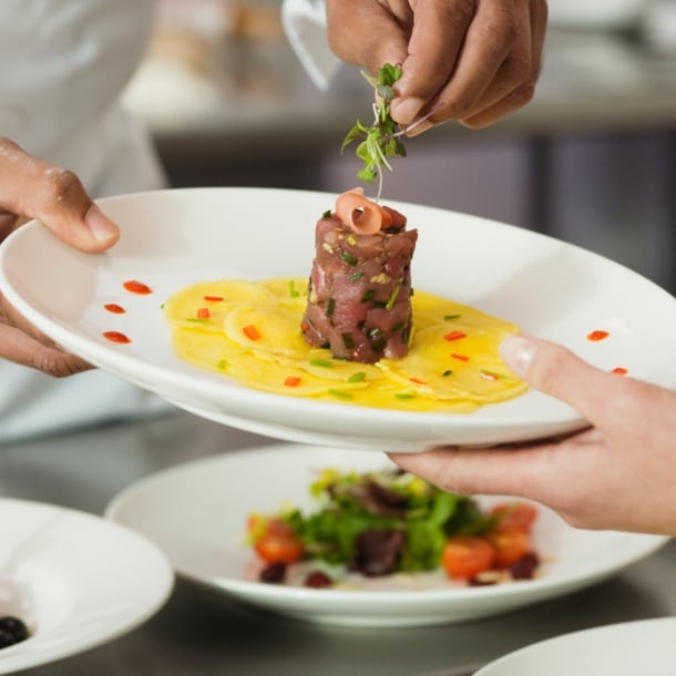 Ein Koch garniert ein Gericht mit Thunfischtartar auf einem weißen Teller in einer Restaurantküche.