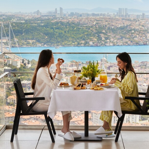Zwei Frauen frühstücken an einem Tisch auf einem Balkon mit Aussicht auf Istanbul.