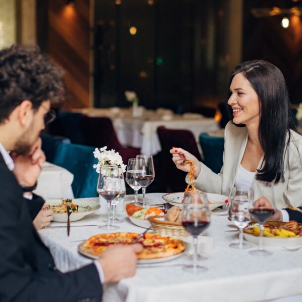Vier elegant gekleidete Personen sitzen beim Essen an einem Tisch in einem Restaurant.