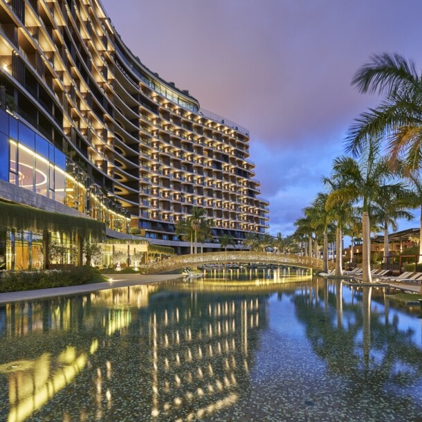 Blick auf ein beleuchtetes Luxushotel mit Palmen und Wasserbecken.